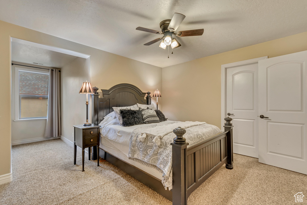 Bedroom with ceiling fan, baseboards, light colored carpet, and a textured ceiling