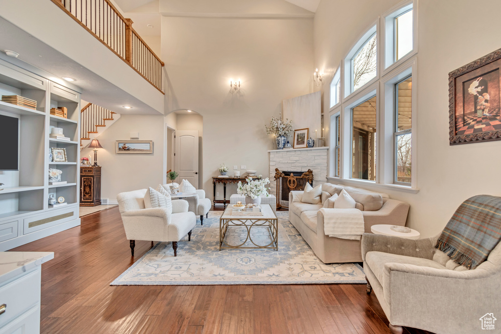 Living room with hardwood / wood-style floors, arched walkways, a high ceiling, and a stone fireplace