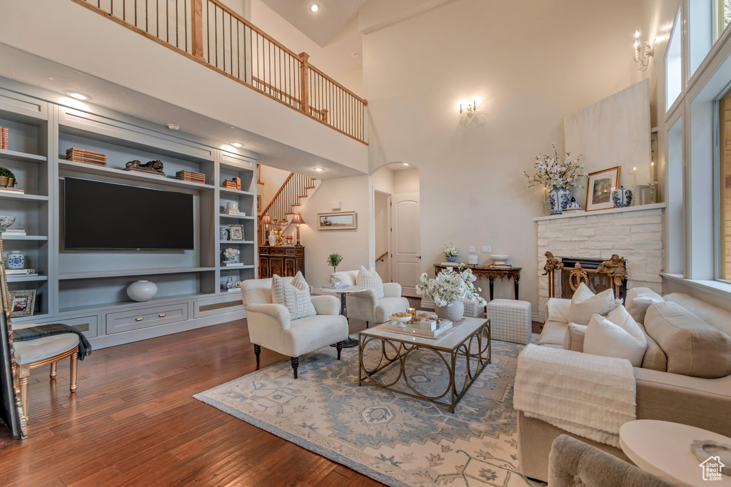 Living area featuring stairs, arched walkways, a stone fireplace, built in features, and wood finished floors