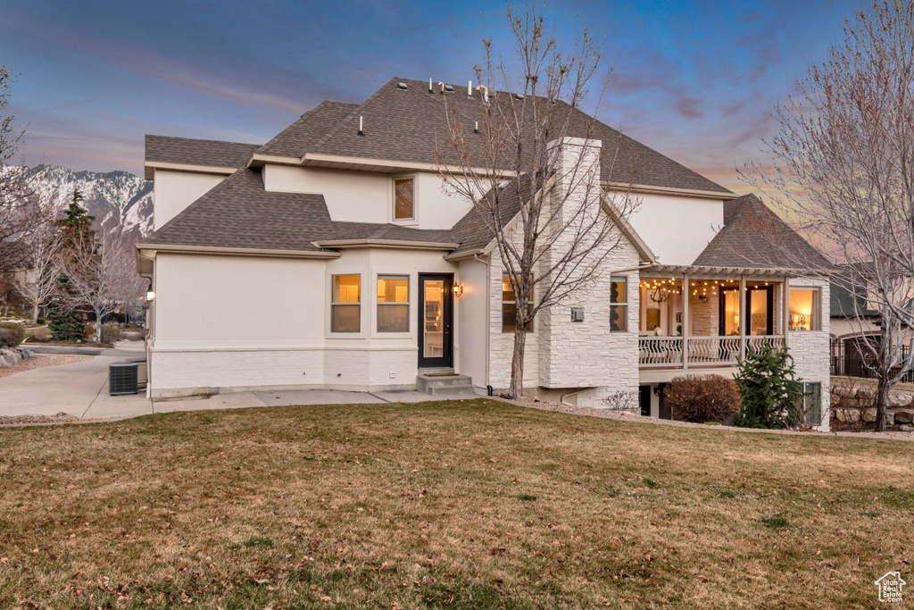 Back of house at dusk featuring a pergola, stucco siding, a yard, and central air condition unit