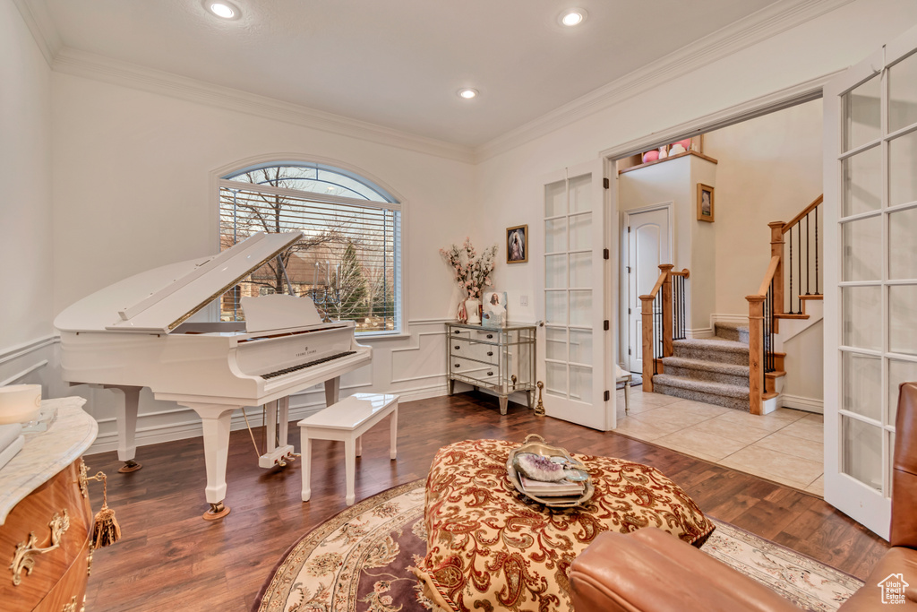 Sitting room with wood finished floors, stairway, ornamental molding, a decorative wall, and wainscoting