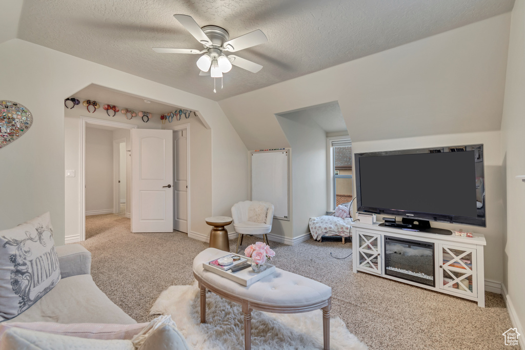 Living room with lofted ceiling, ceiling fan, carpet, and a textured ceiling