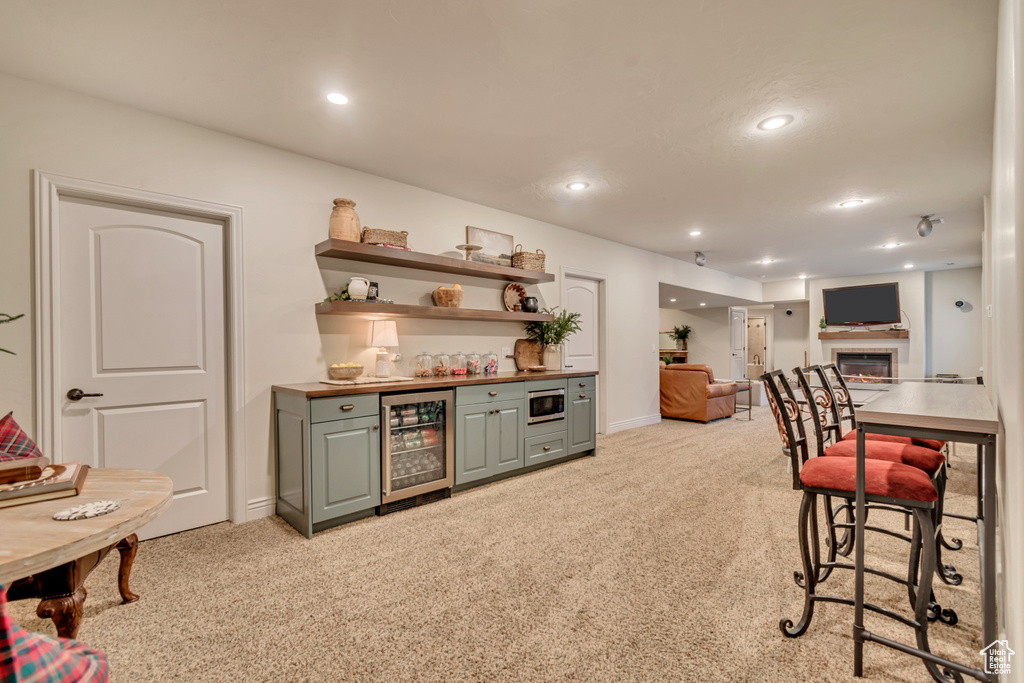 Bar with a bar, beverage cooler, stainless steel microwave, and light colored carpet