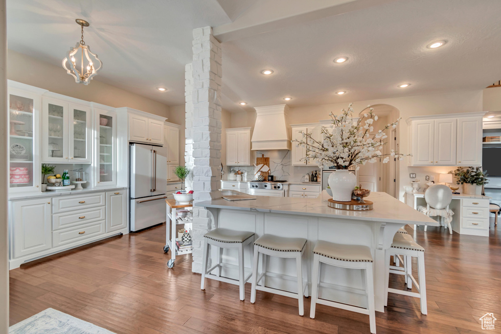 Kitchen with white cabinets, tasteful backsplash, high quality fridge, custom range hood, and stove