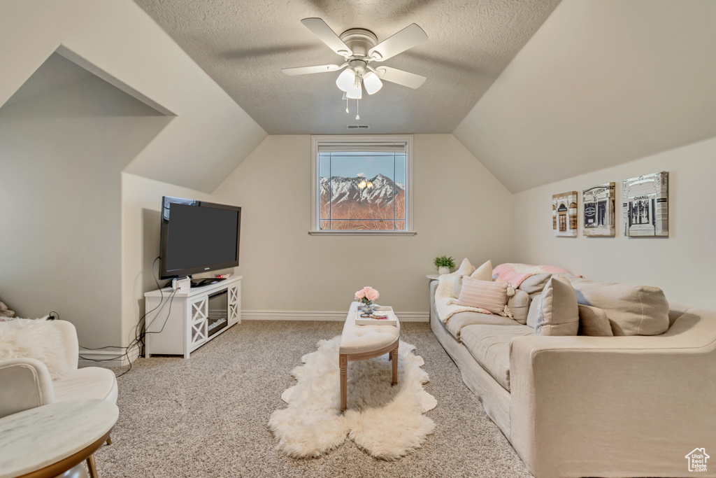 Living room featuring lofted ceiling, baseboards, a textured ceiling, carpet floors, and a ceiling fan