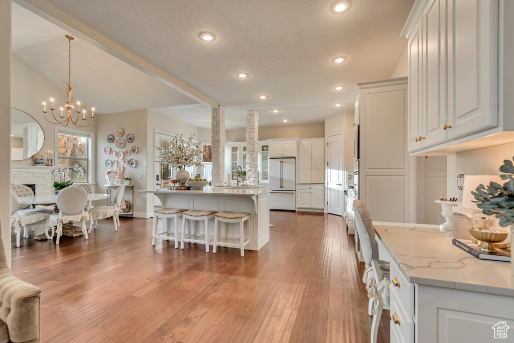 Kitchen featuring white cabinetry, a breakfast bar area, built in refrigerator, a chandelier, and light wood finished floors