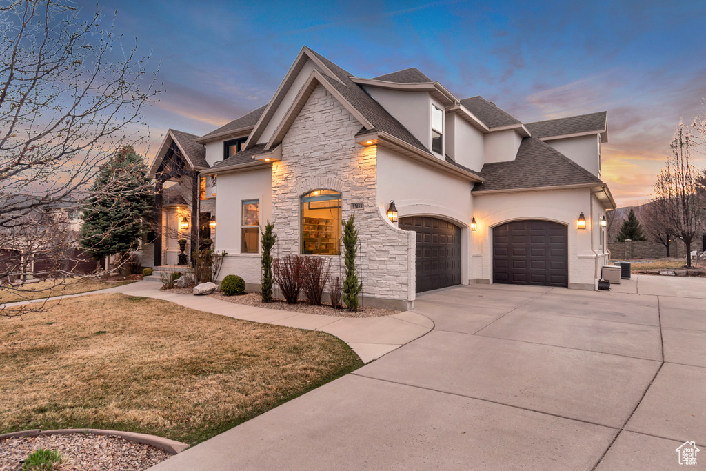 View of front of property featuring a lawn, stucco siding, stone siding, and concrete driveway