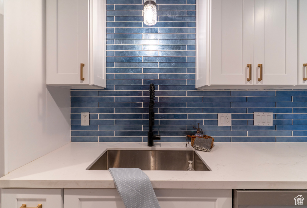 Kitchen featuring white cabinetry, dishwasher, a sink, and backsplash