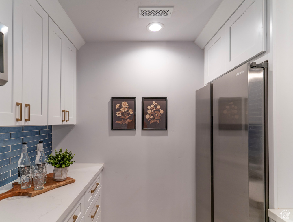 Kitchen featuring white cabinetry, decorative backsplash, light stone counters, visible vents, and freestanding refrigerator