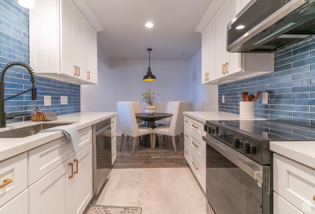 Kitchen featuring light countertops, range hood, a sink, black electric range, and stainless steel dishwasher