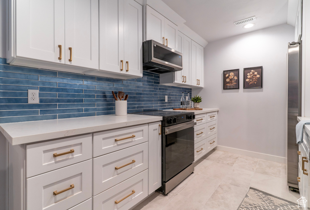Kitchen with baseboards, stainless steel microwave, electric stove, white cabinets, and decorative backsplash