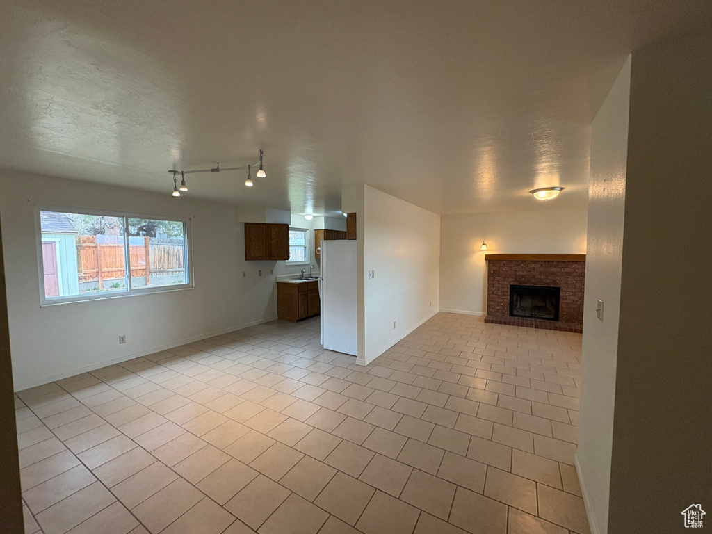 Unfurnished living room featuring light tile patterned flooring, a textured ceiling, a sink, and a brick fireplace