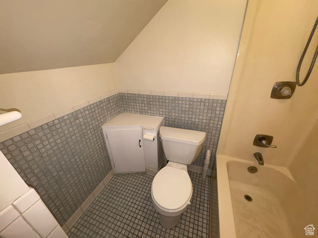 Bathroom featuring tile patterned floors, toilet, shower / tub combination, lofted ceiling, and wainscoting