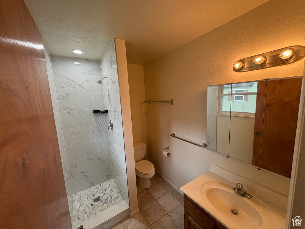 Full bath featuring tile patterned flooring, vanity, toilet, a textured ceiling, and tiled shower