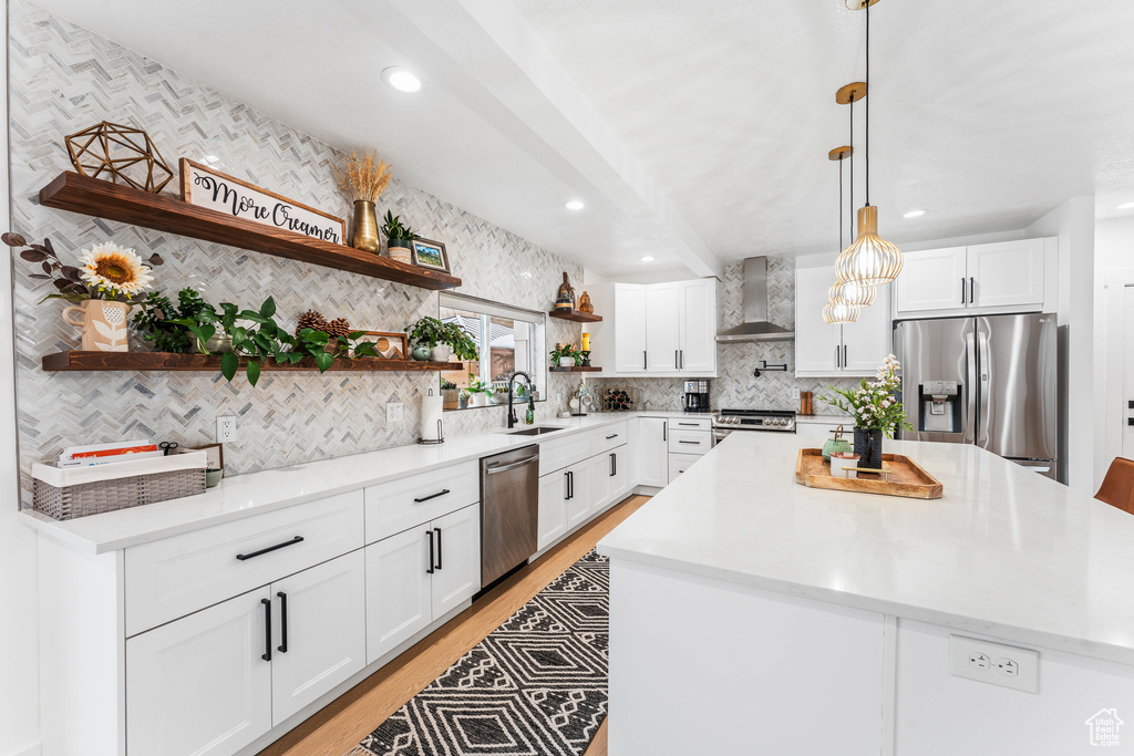 Kitchen featuring a sink, open shelves, light wood-type flooring, stainless steel appliances, and wall chimney range hood