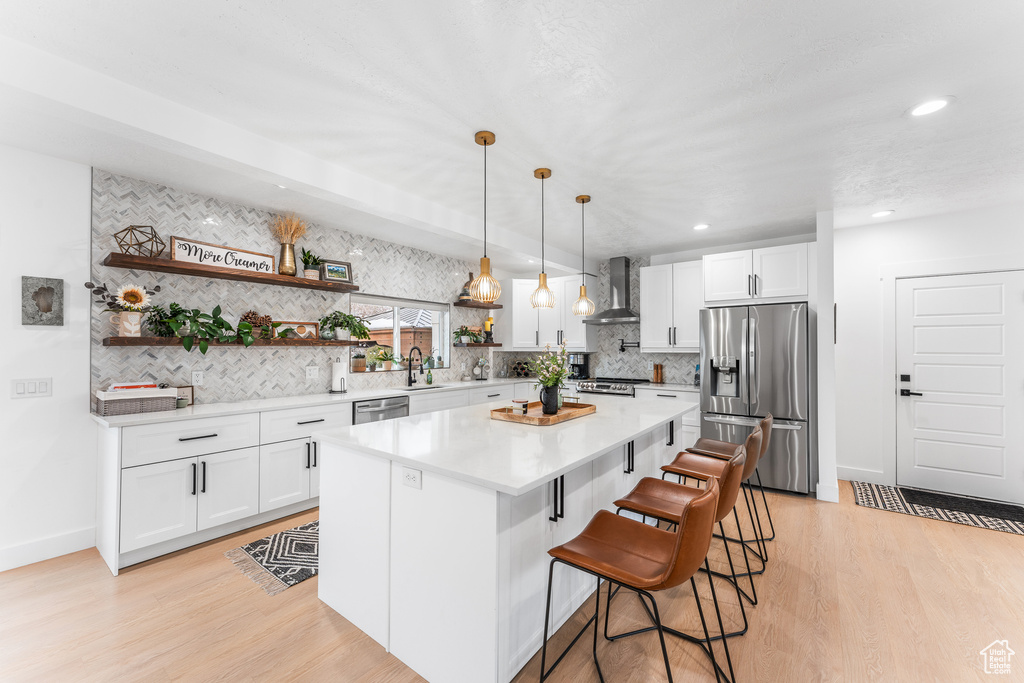 Kitchen with white cabinets, wall chimney exhaust hood, appliances with stainless steel finishes, a sink, and open shelves