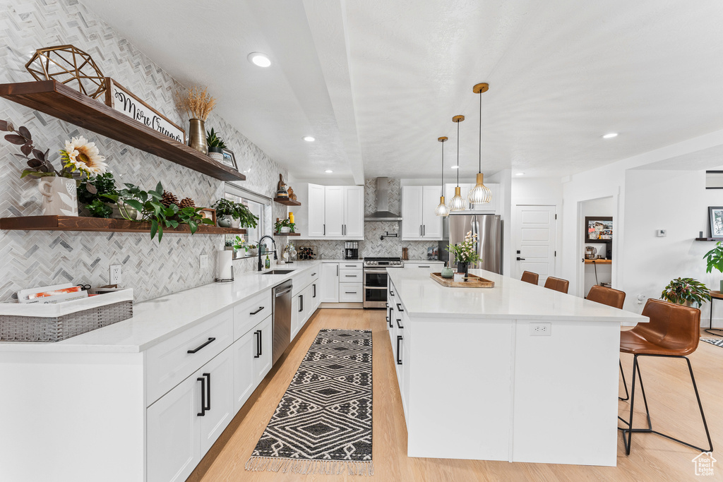 Kitchen featuring a sink, open shelves, wall chimney exhaust hood, a kitchen bar, and appliances with stainless steel finishes