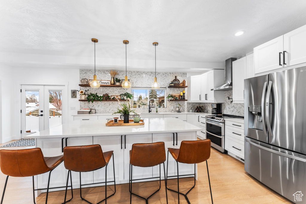 Kitchen featuring light countertops, appliances with stainless steel finishes, open shelves, wall chimney range hood, and backsplash