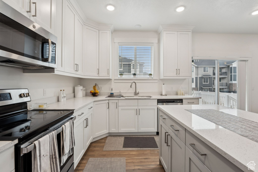 Kitchen with white cabinets, wood finished floors, stainless steel appliances, and recessed lighting