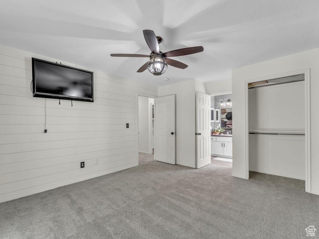 Unfurnished bedroom with carpet, a closet, wooden walls, and ceiling fan