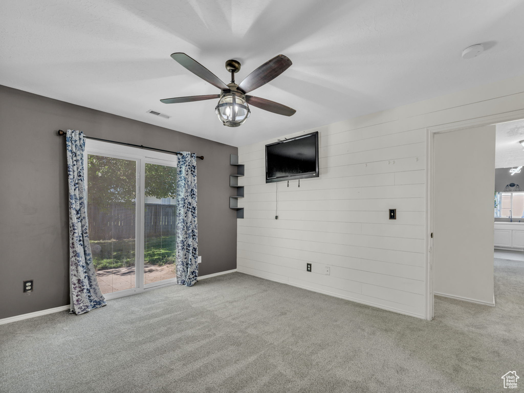 Unfurnished living room featuring ceiling fan, carpet flooring, baseboards, and wood walls