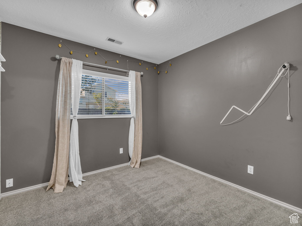Carpeted empty room featuring a textured ceiling and baseboards