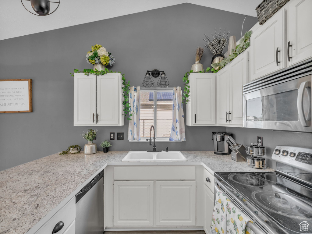 Kitchen featuring stainless steel appliances, a sink, light countertops, white cabinets, and lofted ceiling
