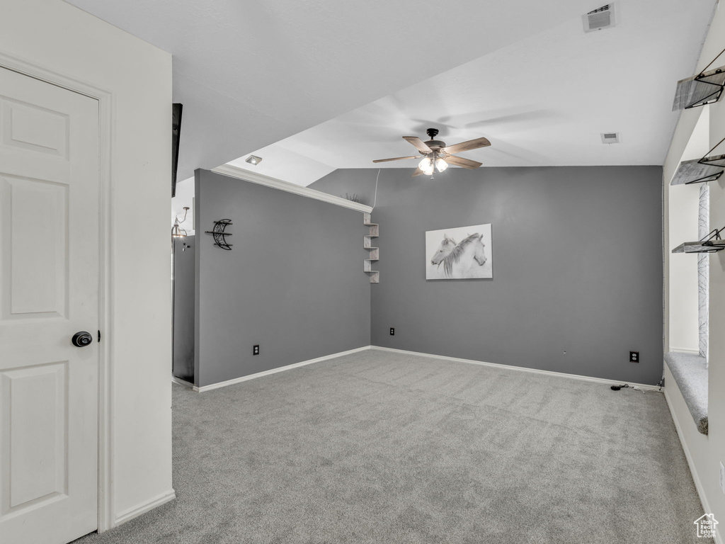 Carpeted empty room featuring ceiling fan, vaulted ceiling, and baseboards