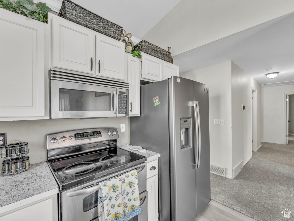 Kitchen with appliances with stainless steel finishes, light countertops, white cabinetry, baseboards, and light carpet