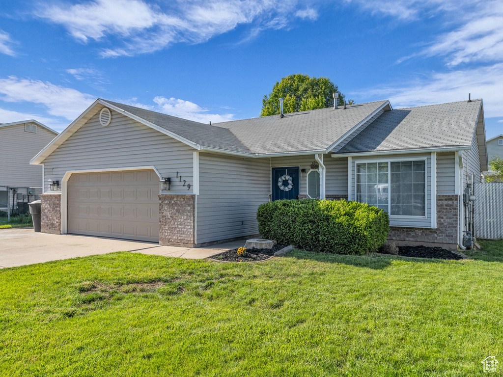 Ranch-style home with an attached garage, concrete driveway, a front lawn, and a shingled roof