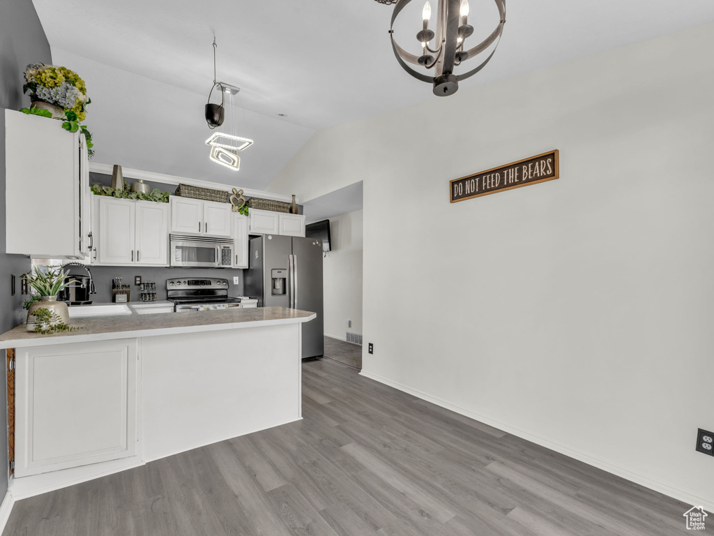 Kitchen featuring appliances with stainless steel finishes, a sink, a peninsula, white cabinets, and a chandelier