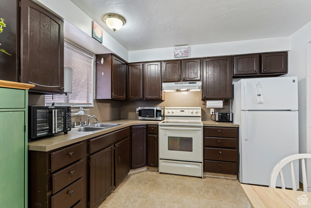Kitchen with light countertops, white appliances, dark brown cabinets, under cabinet range hood, and a sink