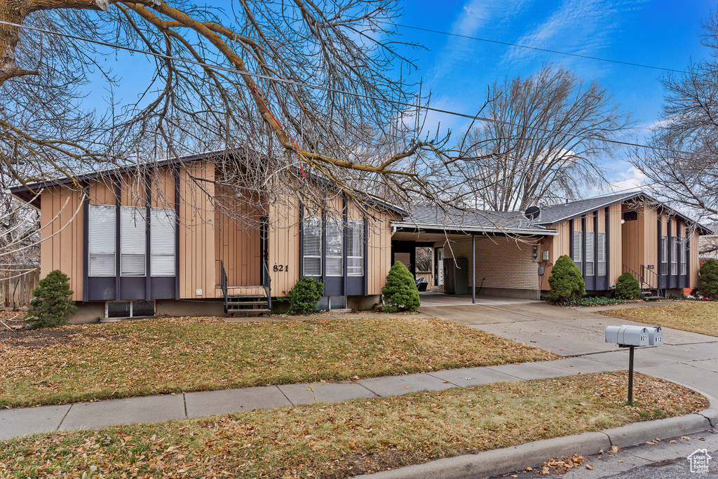 Mid-century modern home with concrete driveway, entry steps, a carport, and a front lawn