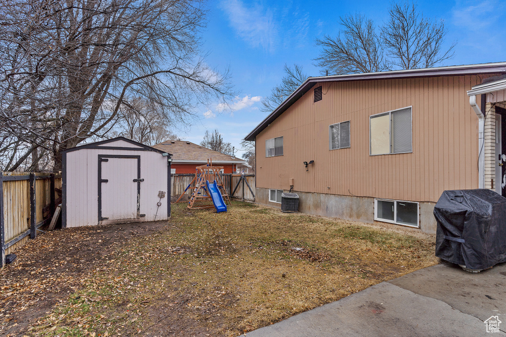 View of home\\\'s exterior with central air condition unit, a playground, a fenced backyard, a storage unit, and an outdoor structure