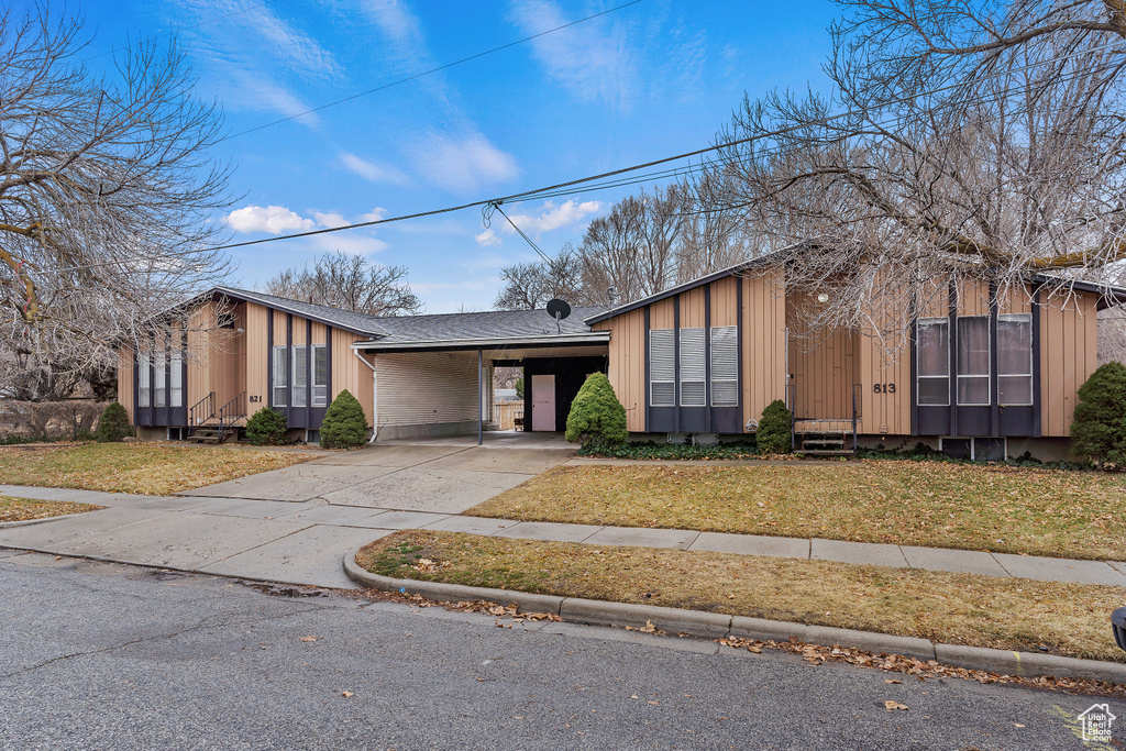 Mid-century inspired home featuring board and batten siding, driveway, entry steps, a front lawn, and a carport