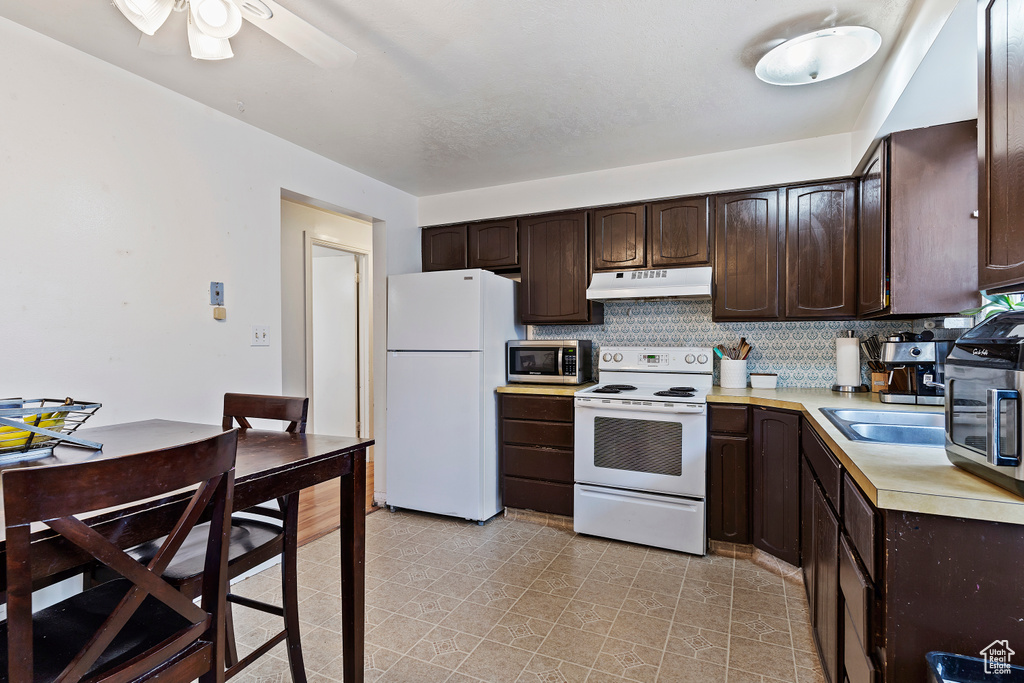 Kitchen featuring decorative backsplash, light countertops, white appliances, dark brown cabinetry, and under cabinet range hood