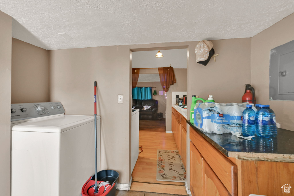 Laundry room featuring electric panel, a textured ceiling, light wood-type flooring, laundry area, and washer / dryer