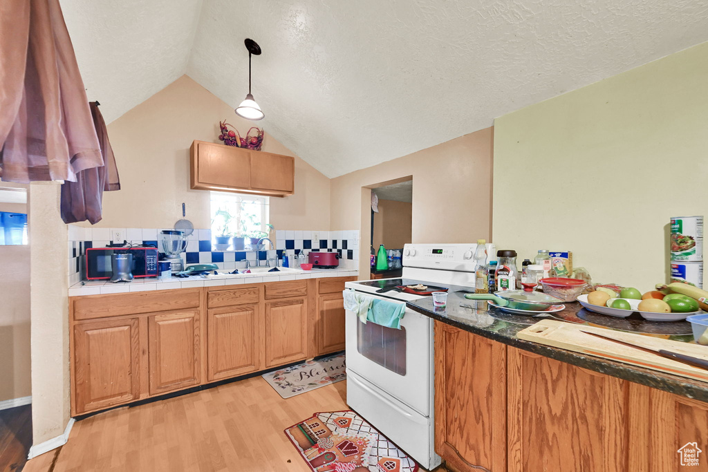 Kitchen featuring lofted ceiling, light wood-type flooring, a textured ceiling, a sink, and white electric range