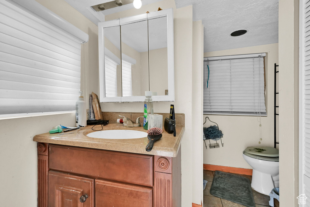 Bathroom with toilet, vanity, a textured ceiling, tile patterned flooring, and baseboards