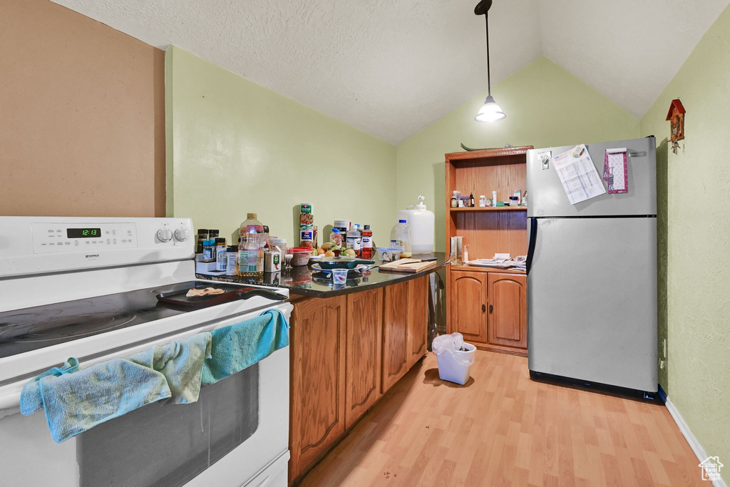 Kitchen with white electric range, light wood-type flooring, vaulted ceiling, brown cabinetry, and freestanding refrigerator