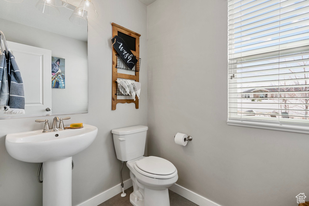 Half bath with toilet, a sink, baseboards, and a healthy amount of sunlight