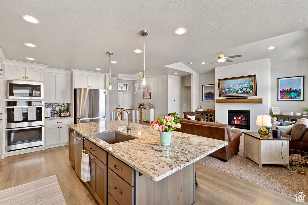 Kitchen featuring appliances with stainless steel finishes, white cabinetry, a sink, light wood-style floors, and open floor plan