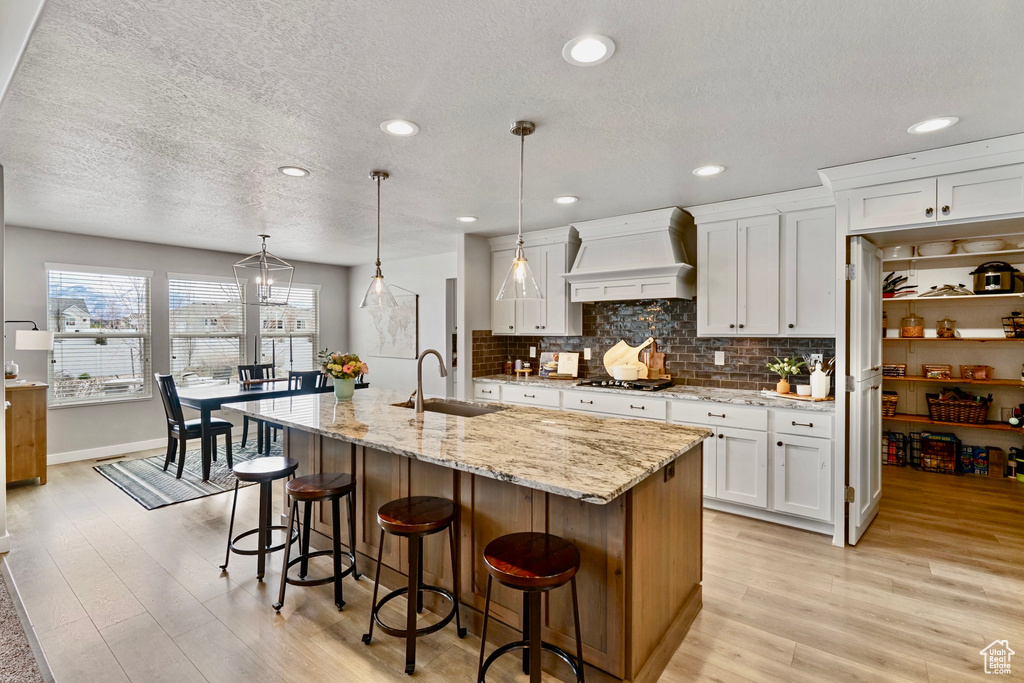 Kitchen with a sink, white cabinetry, a breakfast bar area, light wood-type flooring, and custom range hood
