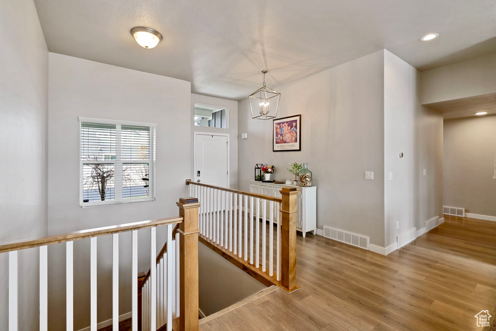 Corridor featuring an inviting chandelier, light wood-style flooring, an upstairs landing, and visible vents