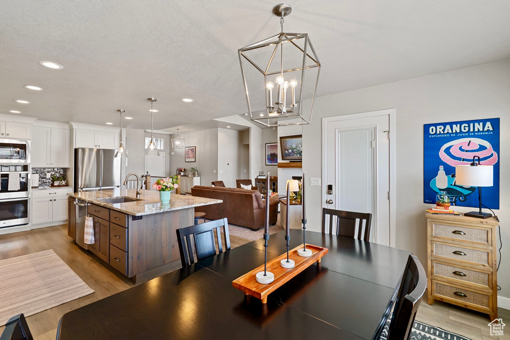 Dining area with a textured ceiling, recessed lighting, light wood-style floors, and a notable chandelier