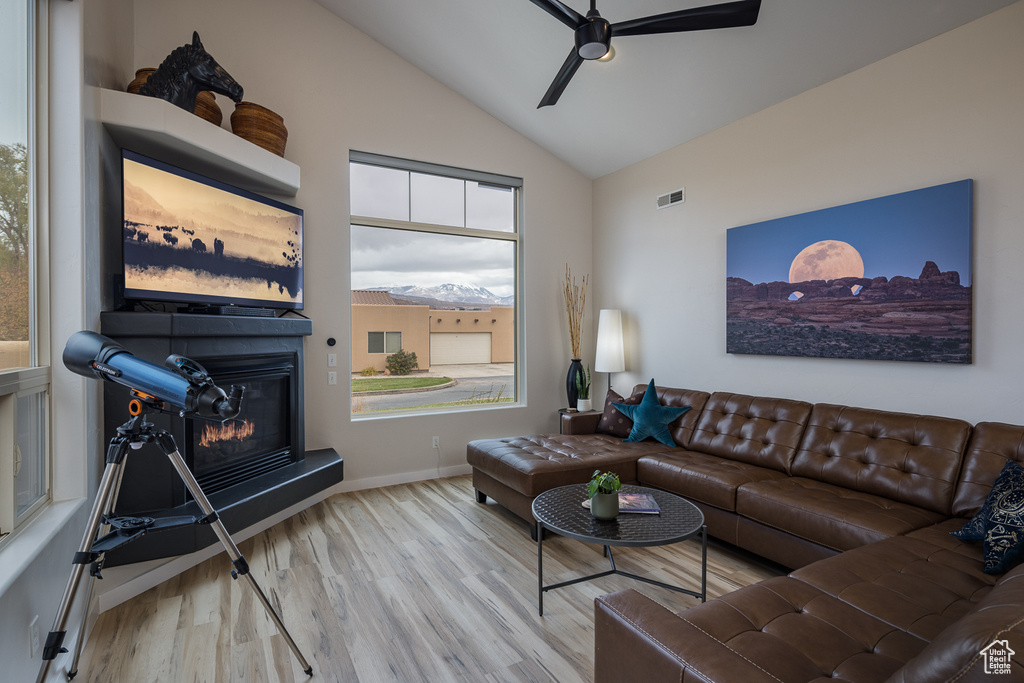 Living area with vaulted ceiling, visible vents, a glass covered fireplace, ceiling fan, and wood finished floors