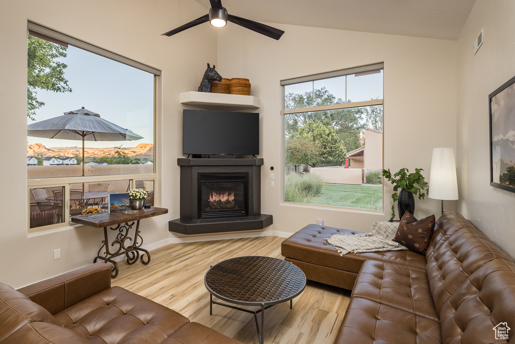 Living area with vaulted ceiling, visible vents, a ceiling fan, a glass covered fireplace, and wood finished floors