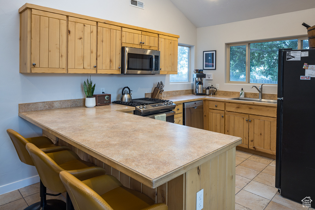 Kitchen featuring lofted ceiling, stainless steel appliances, a sink, a peninsula, and light brown cabinets