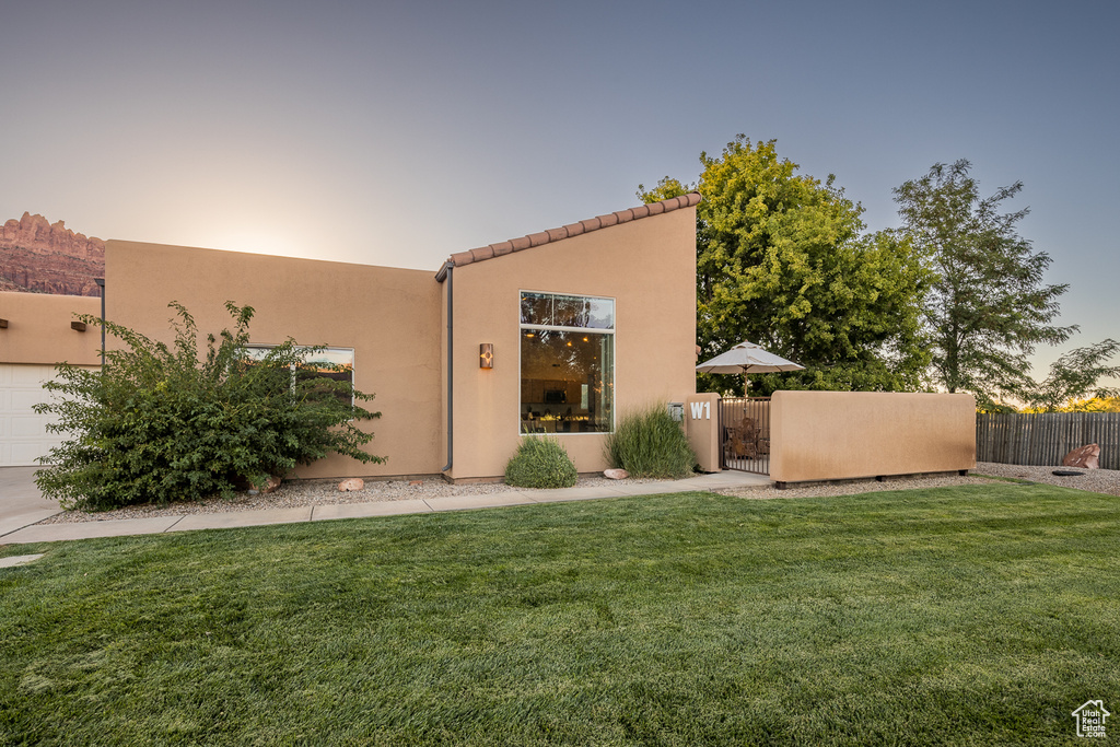 Back of house with a lawn, a gate, fence, and stucco siding