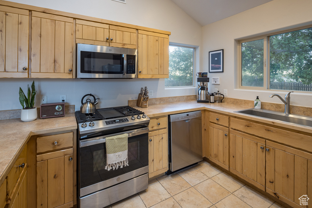 Kitchen with vaulted ceiling, light countertops, a sink, light brown cabinetry, and appliances with stainless steel finishes